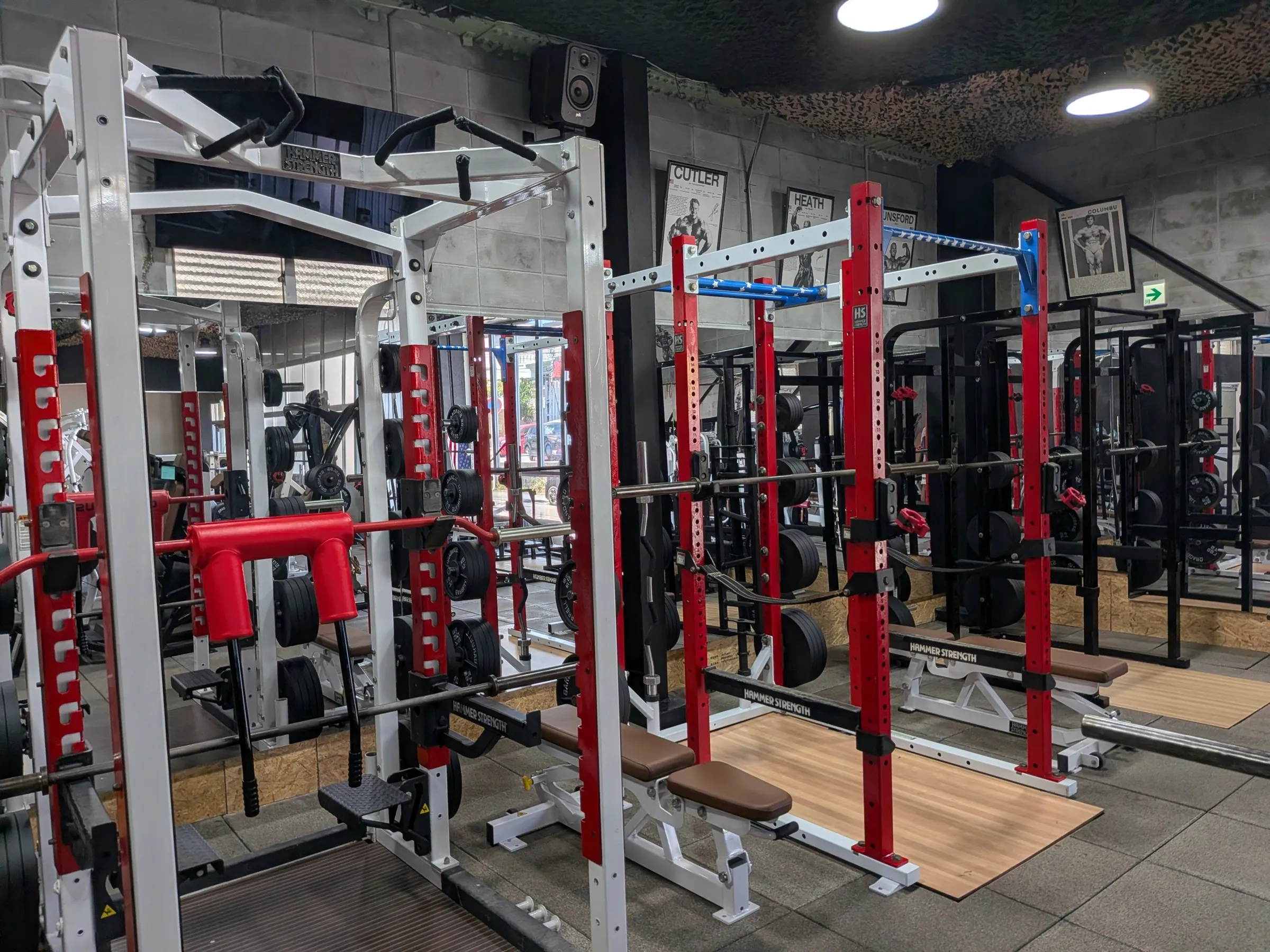 Red and white power racks lined up under camo netting on the Iron Shogun floor